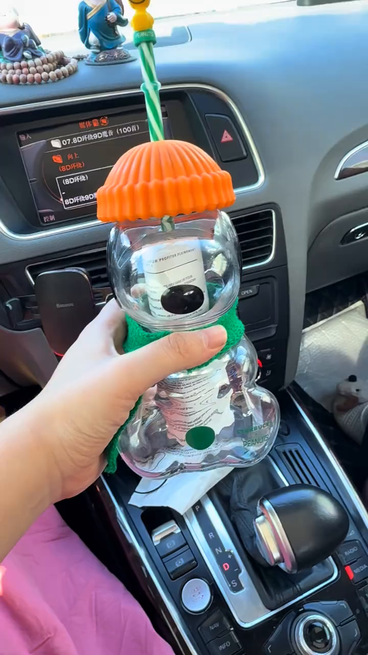 Snoopy glass cup with an orange lid and green scarf held above a car center console.
