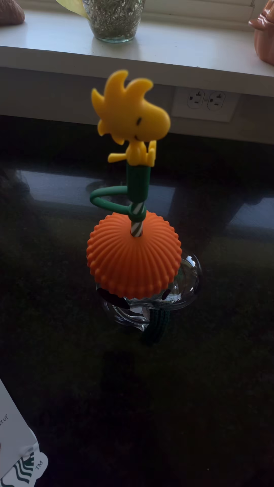 Snoopy glass cup with an orange lid and yellow straw topper beside a kitchen window.
