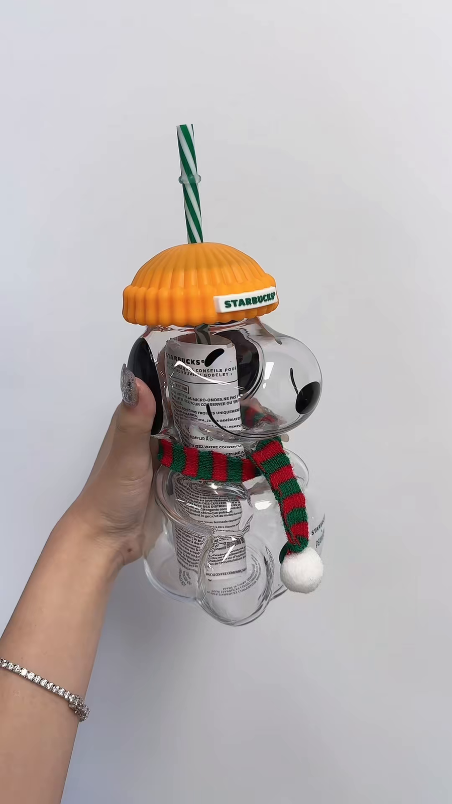 Snoopy glass cup with an orange lid and striped scarf held against a light wall.